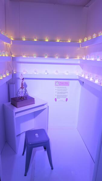 A small room with a white desk and silver stool, with lit, faceted crystals lining the walls