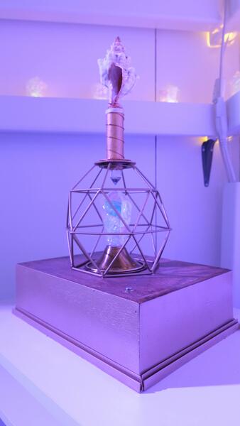 A prop made of a box platform with a cage-like structure on top surrounding a crystal, and a shell sitting above that on a small metallic tube