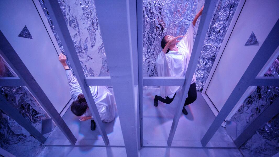 Two performers inside a reflective room, mirroring each other's movements