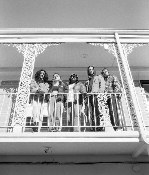 The band Doubt standing in a line on a balcony at a motel. Photo is taken from below as the subject look down. Black and White