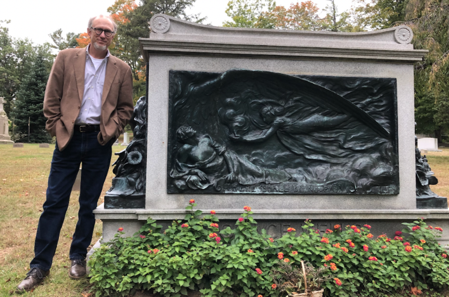 The author in brown coat and jeans stands next to the tombstone for Horace Wells and his family, which features a bas-relief sculpture of an angel carrying pain-numbing vapors from heaven to a suffering man.