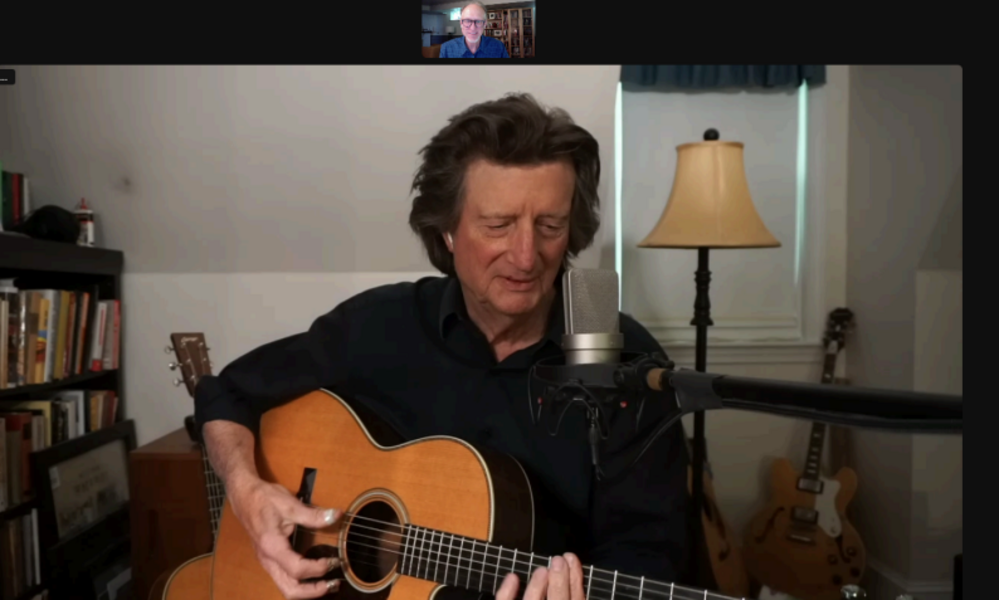 A screen capture of a Zoom conversation featuring the author as a small headshot atop the image of a black-clad man playing guitar