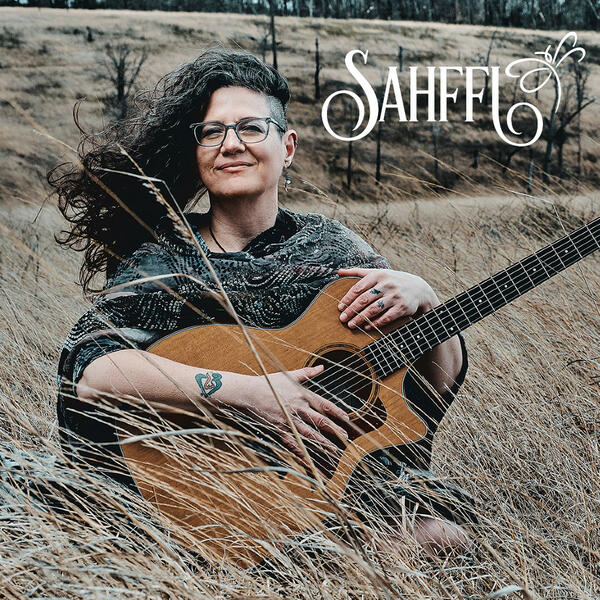 Sahffi sitting in a field with guitar with Logo