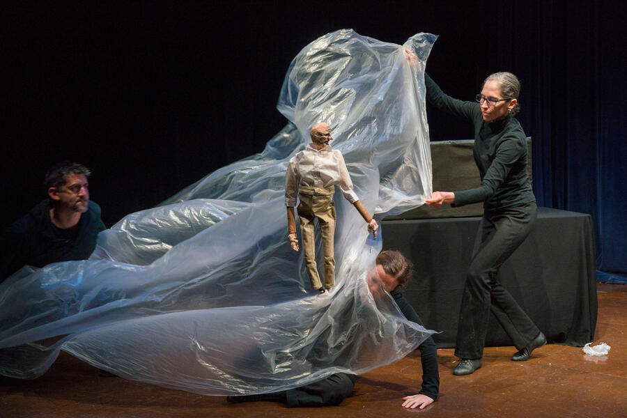 Four puppeteers manipulate a large piece of plastic to represent a tidal wave in a performance.