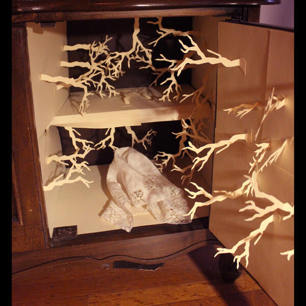 An open cabinet reveals branch silhouettes made of paper and attached to the walls inside.