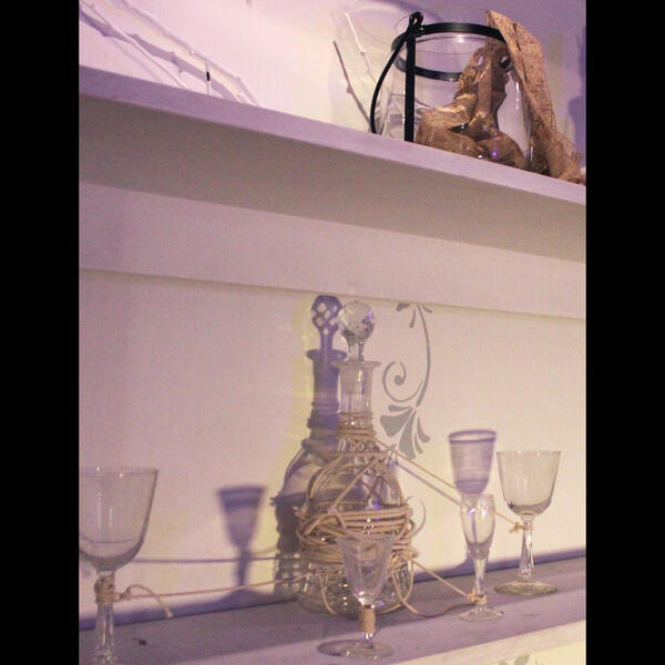 A shelf with a crystal decanter and delicate wine glasses all bound together with thick rope.