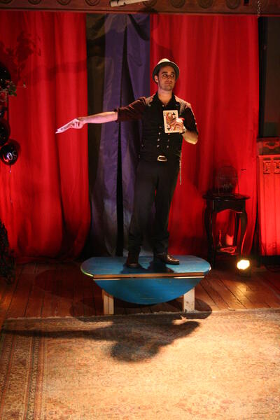 Magician stands center stage with large cards.
