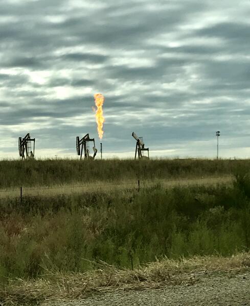 Image of three oil derricks and a pipe flaring (releasing natural gas) into the air, causing a large flame