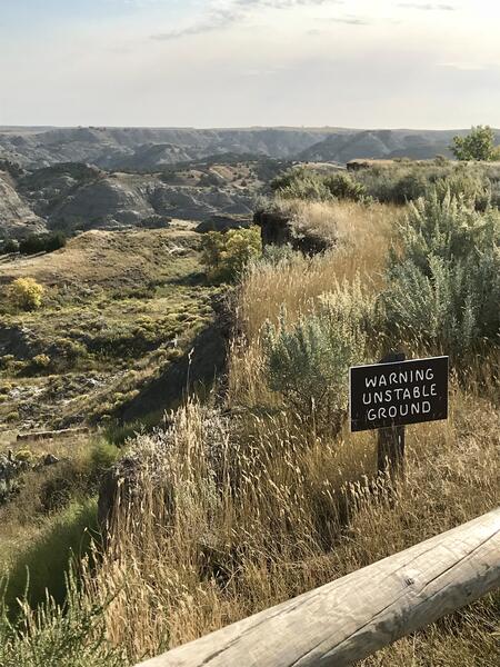 Image of a wide valley in the national park and a sign that reads, "Warning, Unstable Ground"