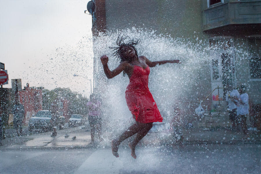 photograph of woman in red dress jumping in open fire hydrant spray
