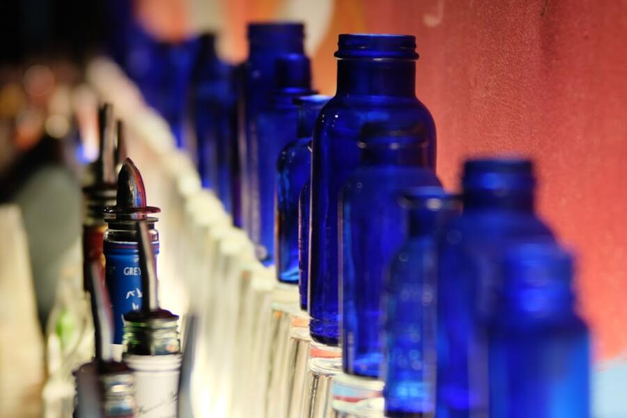 a number of unmarked cobalt blue medicine bottles are lit from below and sit atop a bar.