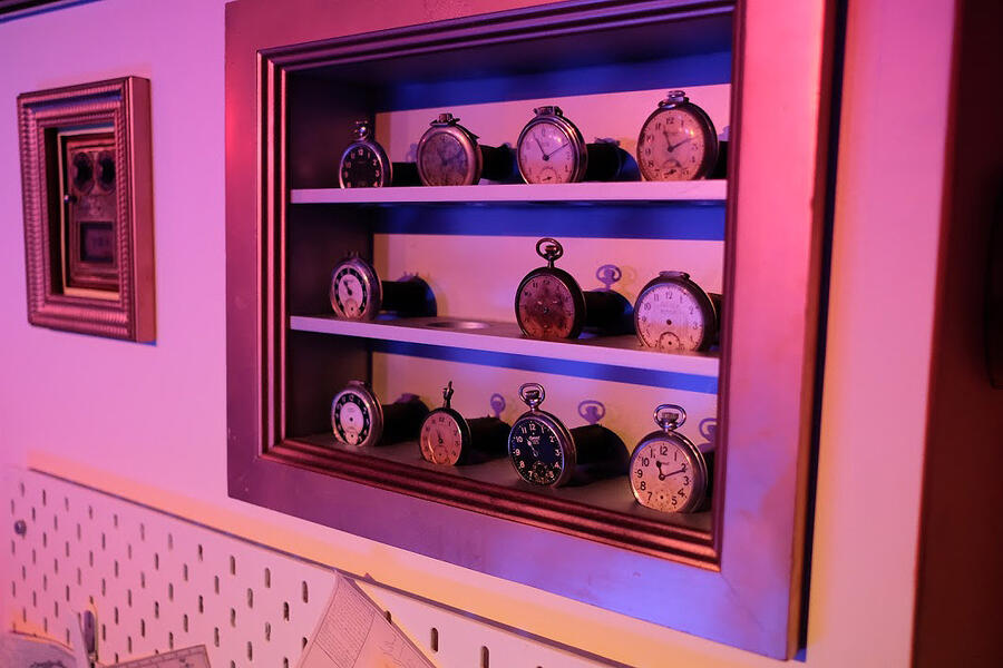 A small shelf inset into a wall displays eleven pocket watches of varying sizes.
