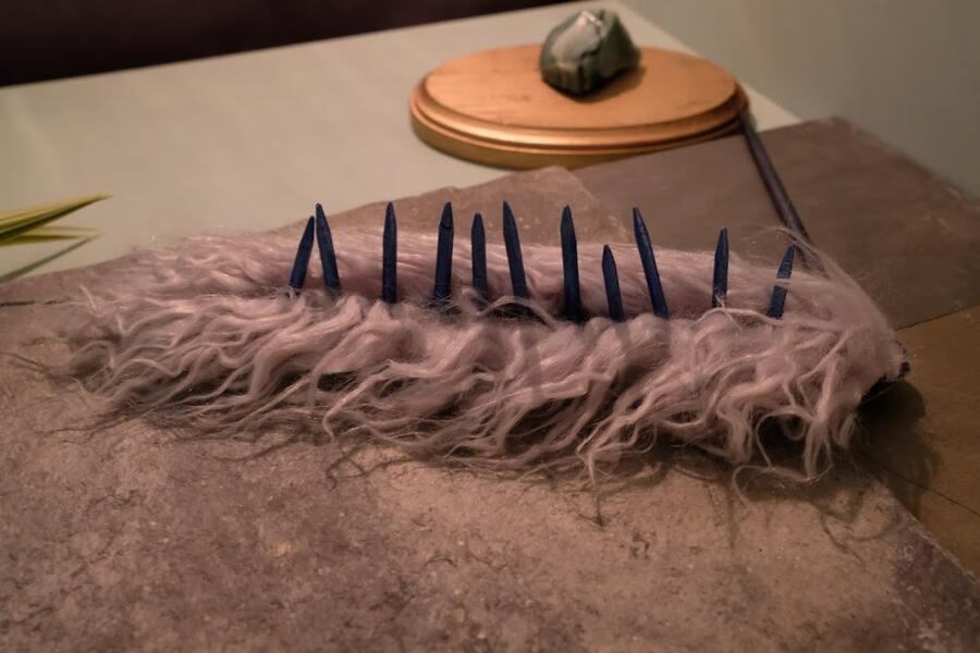 A puppet, representing an otherworldly species, appears to be a furry, blue slug-like dark blue spikes sticking up along its back.