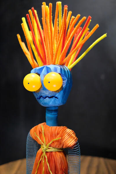 A tabletop puppet, with orange and red hair standing straight up and bulging yellow eyes, representing generalized anxiety, sits atop a bar table.