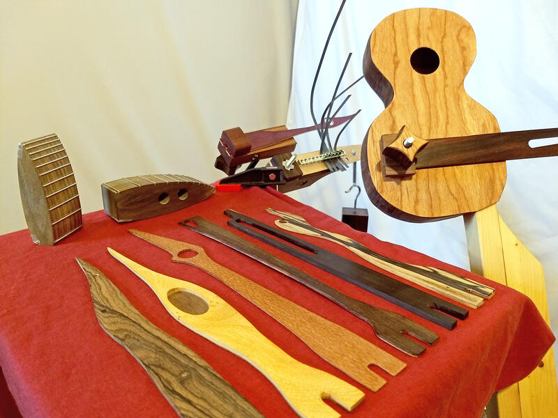 Display of daxophone tongues (foreground), daxes (left), daxulele (right), desk mounted daxophone with kalimba tongue (center), and tripod daxophone (center, rear).
