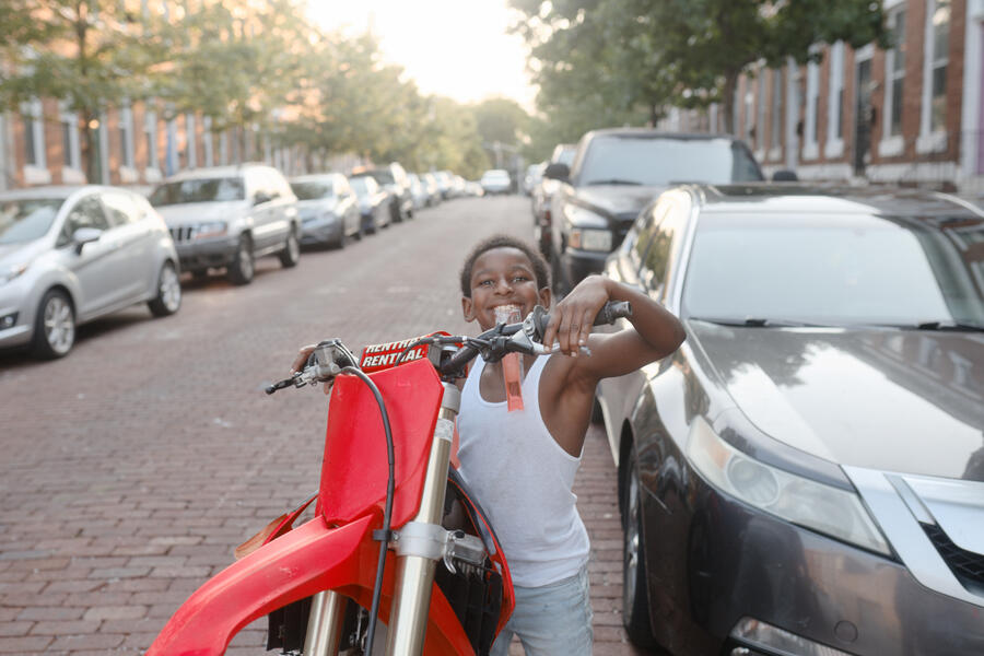 A boy eats a popsicle on his brother's dirt bike in Harwood.