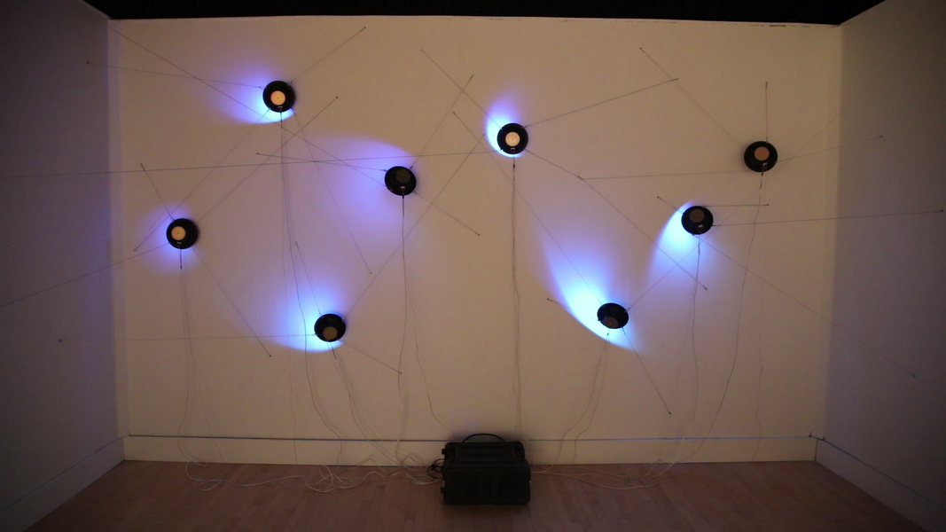 an image of 8 speakers hung against a wall, with LEDs in their cones illuminating the wall