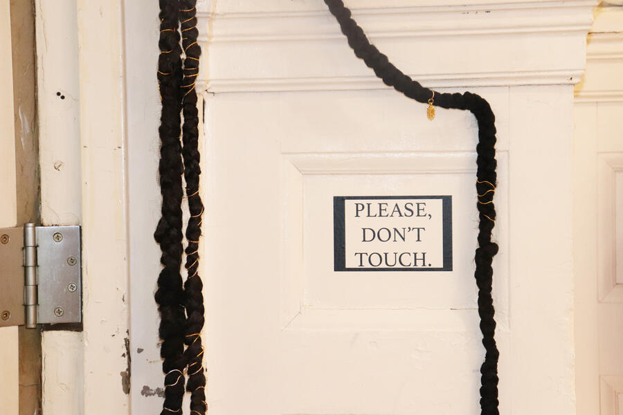 Braids hanging over the exhibition entrance with vinyl that reads "PLEASE, DON'T TOUCH."