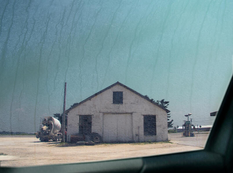 Image of white building with cement truck next to it shot through a streaky car window.
