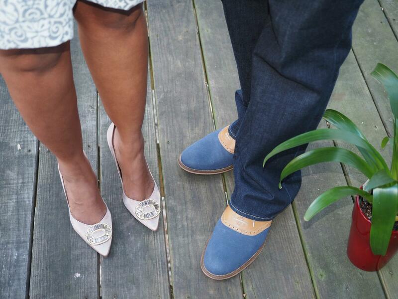 Pamela Woolford's legs and the bottom portion of her knee-length white and silver dress, wearing bejeweled high heels, next to the legs of her now ex-husband in dark denim and blue and tan oxford shoes. They are standing on the wooden planks of a deck.