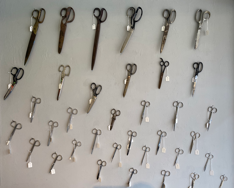 An array of Tailor's Scissors hanging on a wall with name tags hanging off them