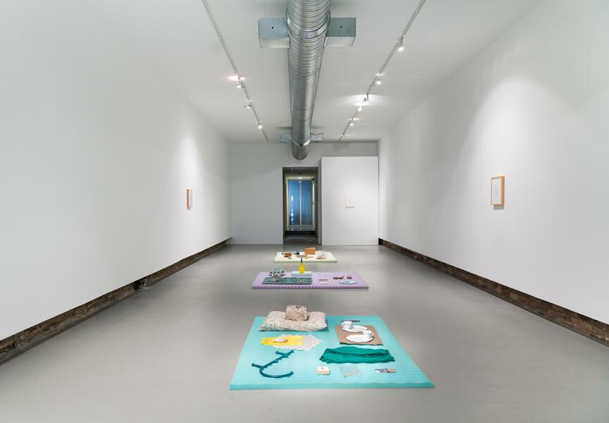 Gallery installation of brightly colored sculptures on the floor and small framed objects on white walls