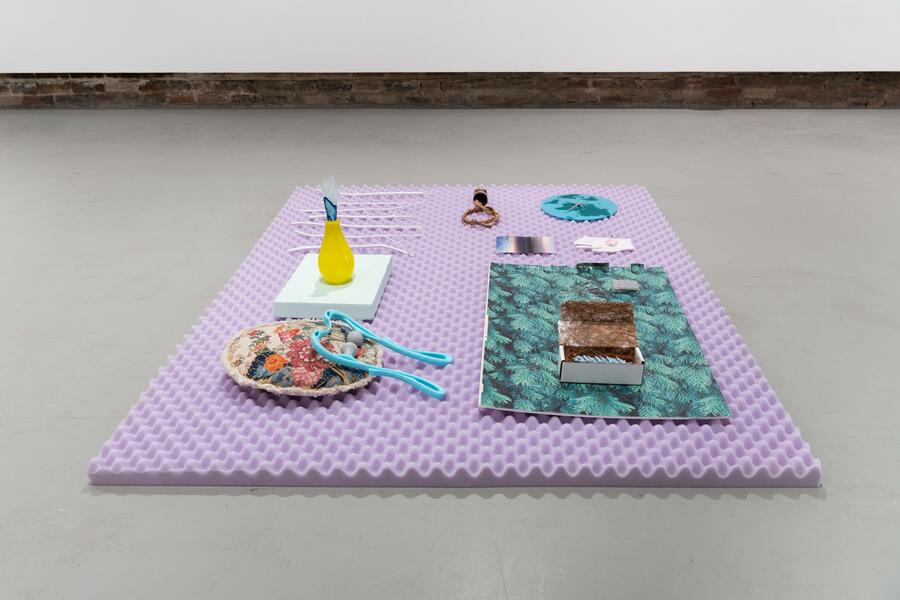 Found objects arranged neatly on top of a lavender-colored mattress topper on a gray floor