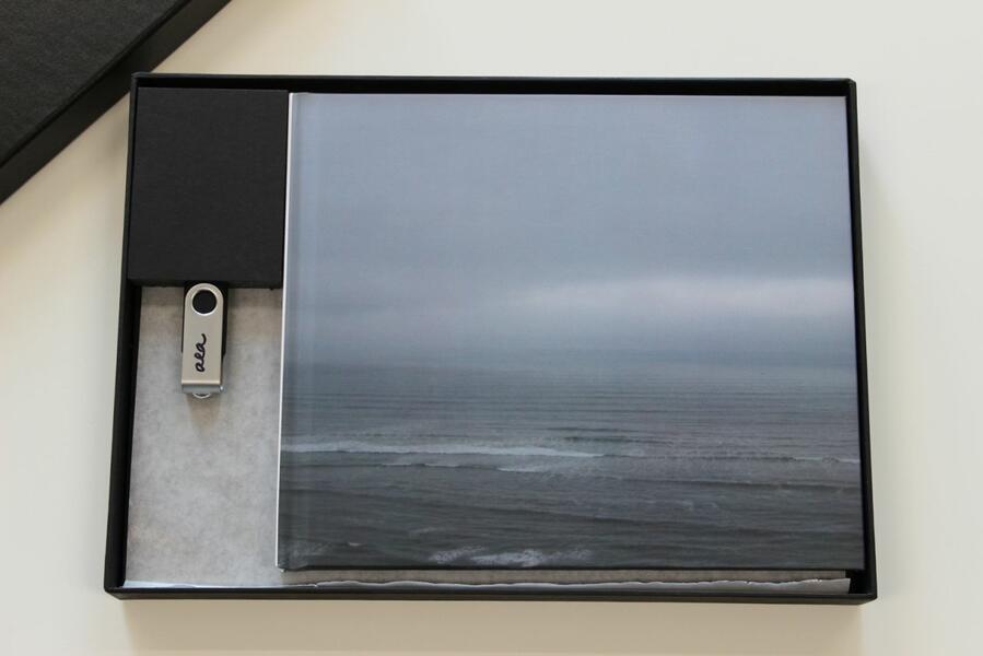 Book with an image of a gray sea and sky inside of a box with a flash drive beside it
