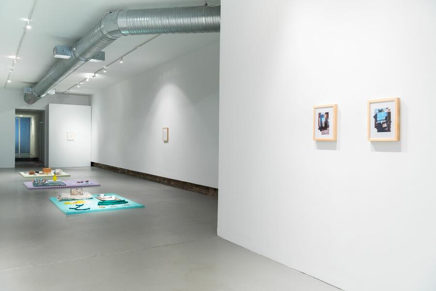 Two small framed works on a white wall with sculptural floor works in the background