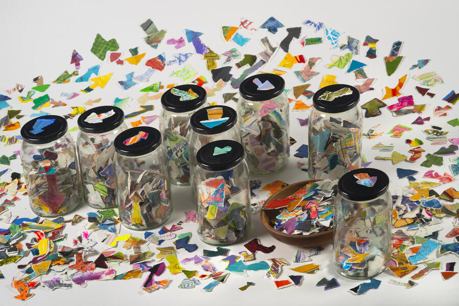 Hand-torn arrows from old paintings are scattered on a surface and in multiple glass jars with lids.