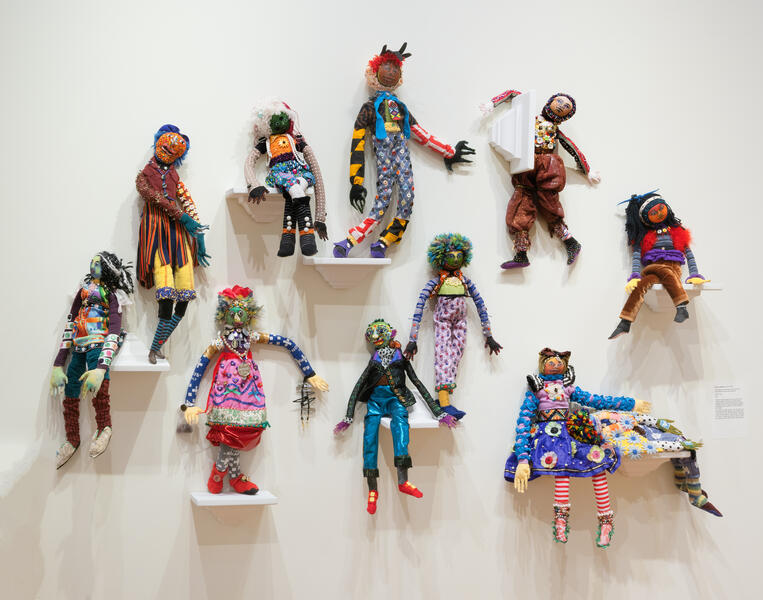 Eleven hand-sewn figures on shelves made from recycled and repurposed materials.
